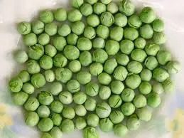 A pile of green peas on top of a white plate.