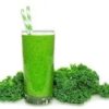 A glass of green juice with some leaves on the ground