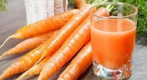 A glass of juice and some carrots on the table