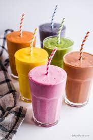 A group of five glasses filled with different colored smoothies.