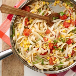 A pan of noodles with corn and tomatoes.
